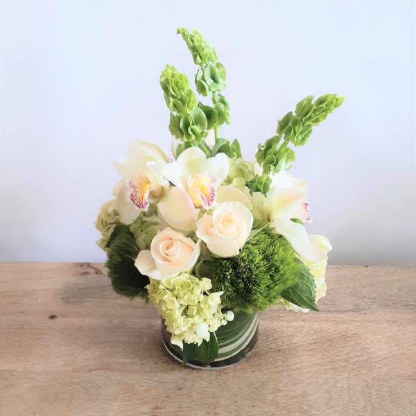 Cream roses and white orchids arranged in a glass vase with green blooms