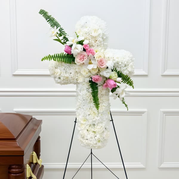 White funeral spray with pink roses and lilies on a stand beside a casket