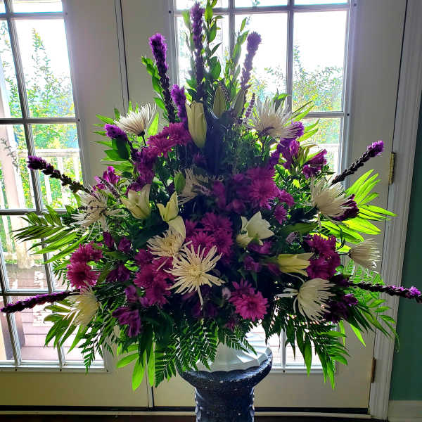 Large purple and white floral arrangement in a pedestal vase