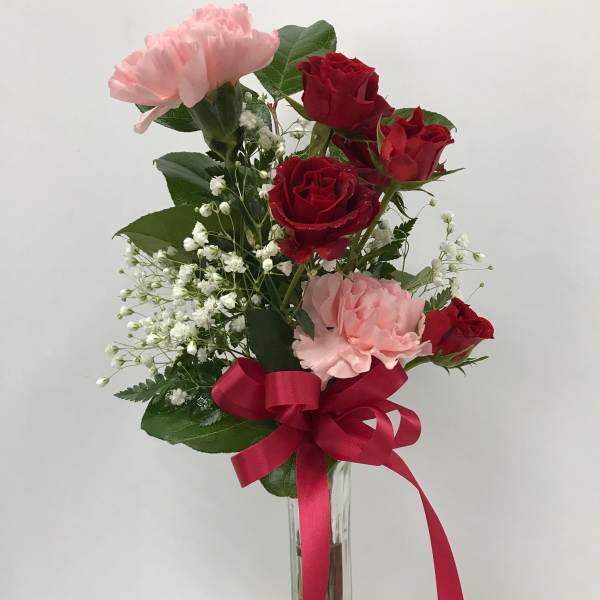 Red roses and pink carnations in a clear glass vase with a red ribbon