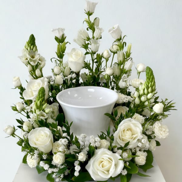 White roses and mixed white flowers arranged around a white urn vase