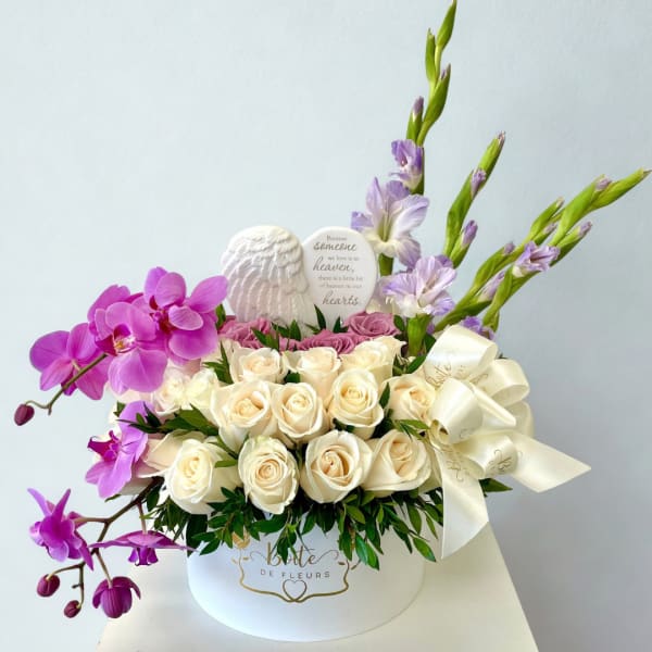 White roses and purple orchids arranged in a round hat box with a ribbon