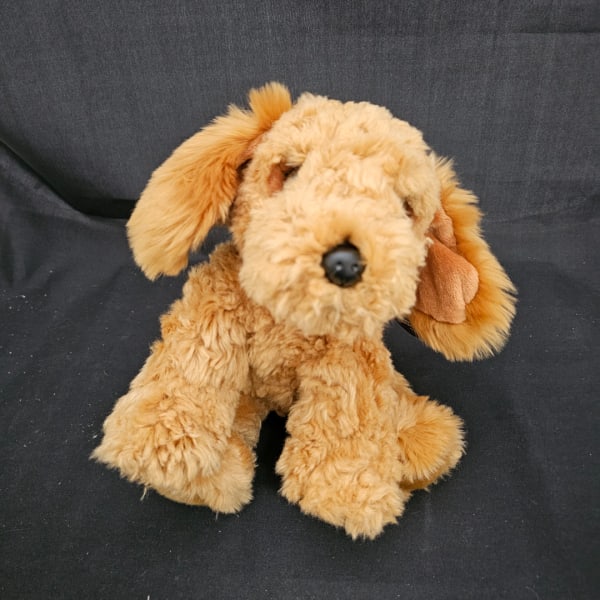 Plush tan dog toy sitting on a dark fabric background