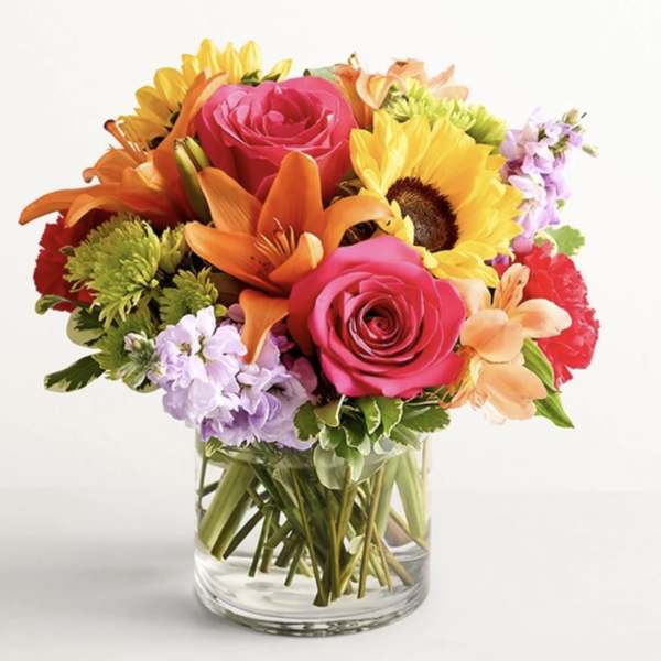 Mixed bouquet of roses, lilies, and sunflowers in a clear glass vase