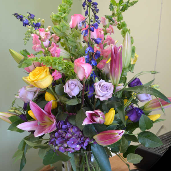 Mixed bouquet of roses, lilies, hydrangea, and blue flowers in a glass vase