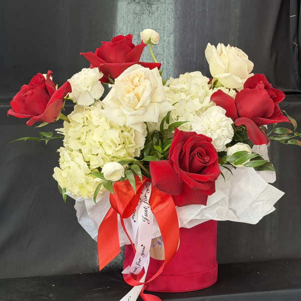 Red and white roses arranged in a pink hat box with a ribbon