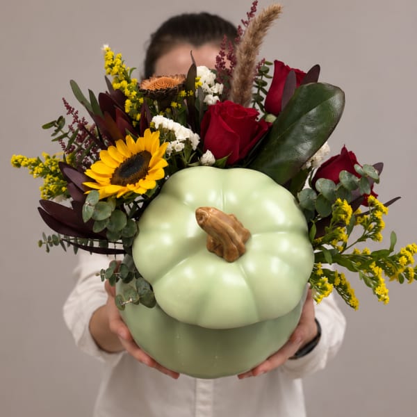 Mixed bouquet in a pale green pumpkin-shaped container with red roses and a sunflower