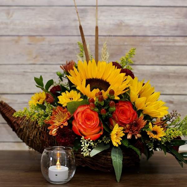 Sunflower and rose arrangement in a wicker basket with a small candle in front