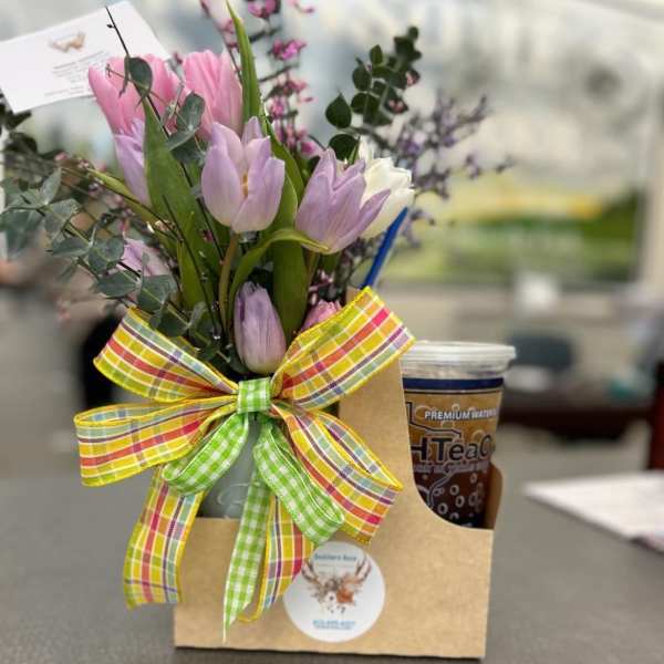 Gift caddy with pastel tulip bouquet, plaid bow, and iced tea cup on a table