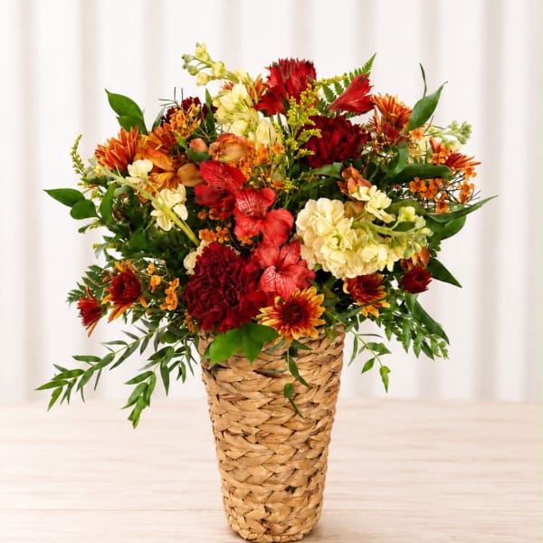 Mixed bouquet of red, orange, and cream flowers in a woven basket vase