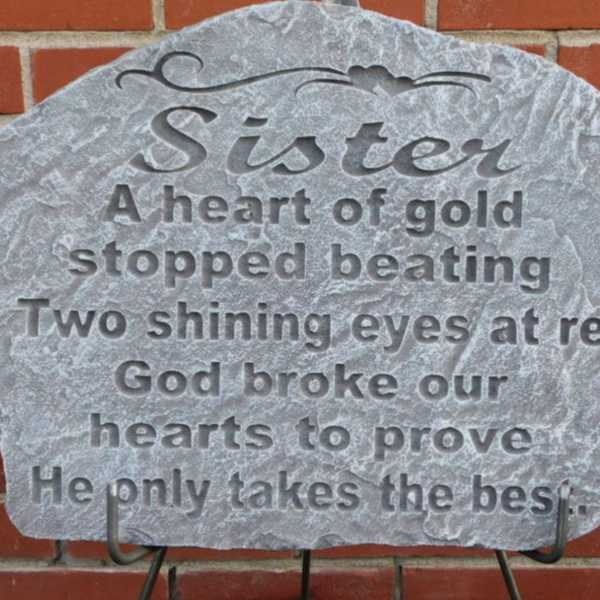 Gray memorial plaque with engraved tribute text against a brick wall