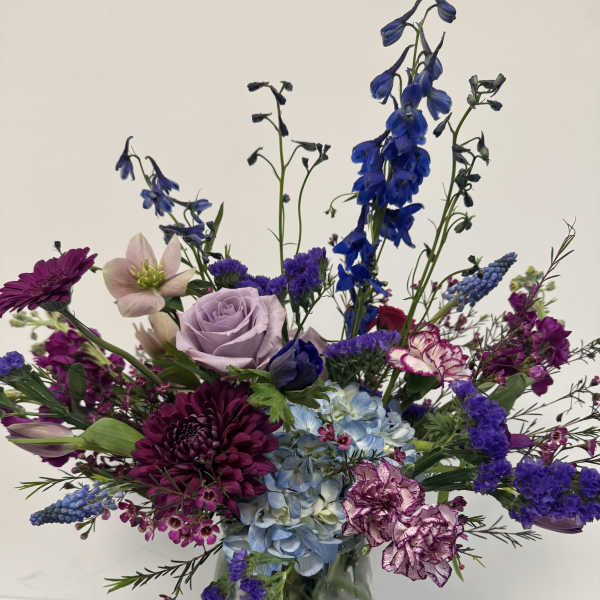 Mixed purple and blue flowers arranged in a clear glass vase