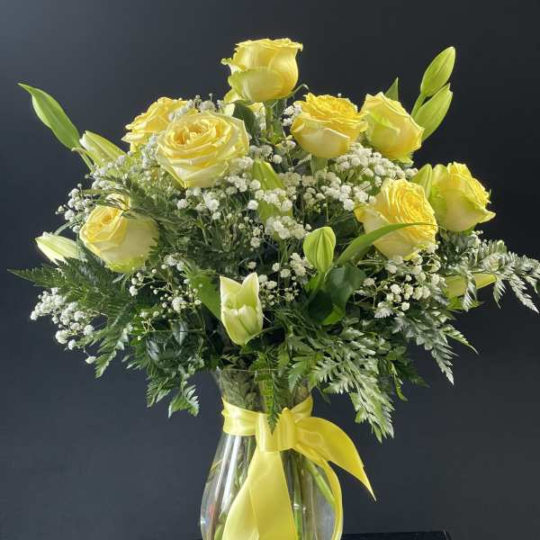 Yellow roses and lilies in a clear glass vase with a yellow ribbon