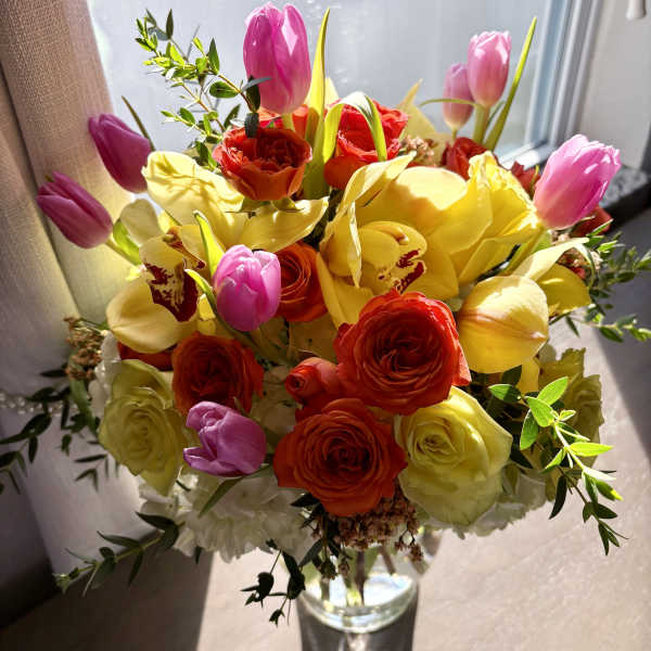 Bouquet of pink tulips, yellow orchids, and red roses in a glass vase