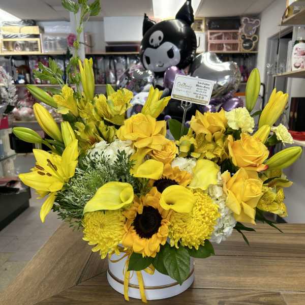 Yellow floral arrangement with lilies, roses, sunflowers, and calla lilies in a white box