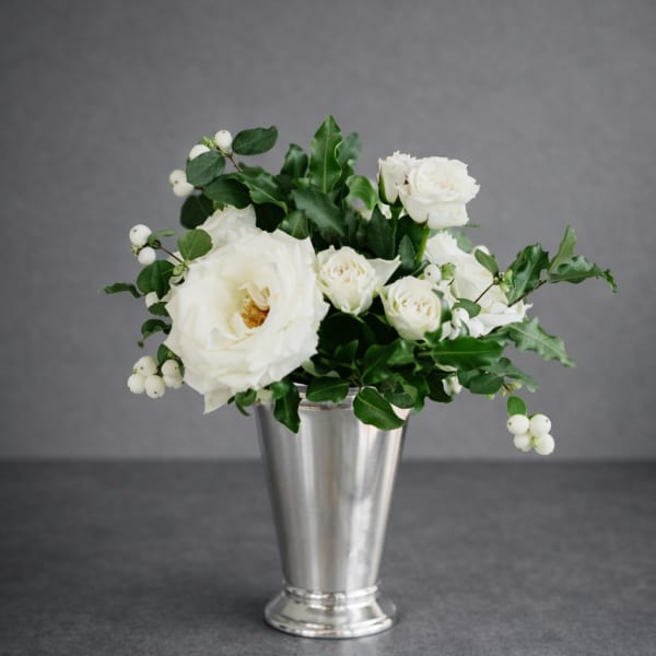 White roses and berries arranged in a silver vase
