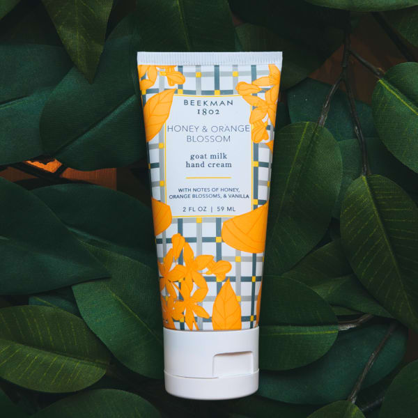 Tube of honey and orange blossom hand cream on dark green leaves