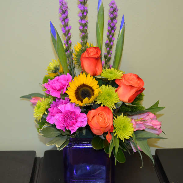 Colorful mixed bouquet in a purple glass vase with roses and sunflowers