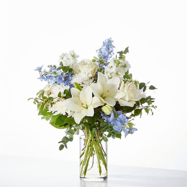 White lilies and roses with blue flowers in a clear glass vase