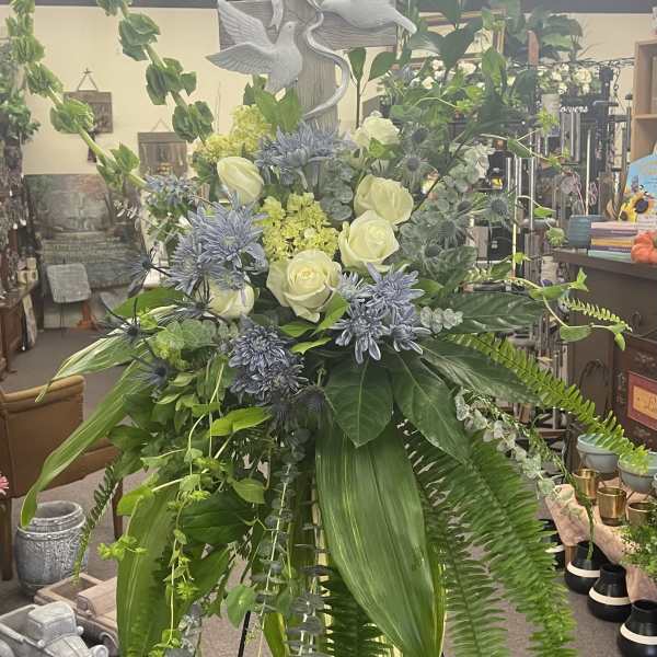 Tall floral standing spray with white roses and blue flowers on an easel
