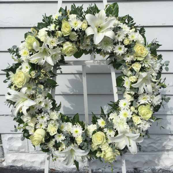 White floral wreath with roses, lilies, and daisies on a stand