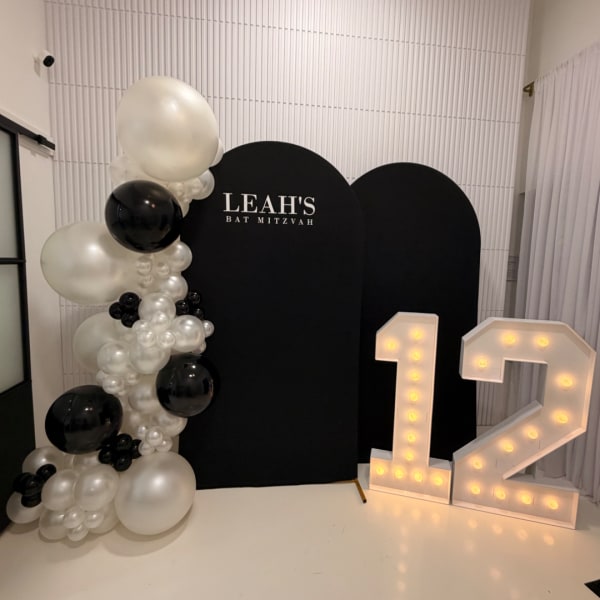 Black and white balloon display with a lit number 12 and Leah's Bat Mitzvah sign