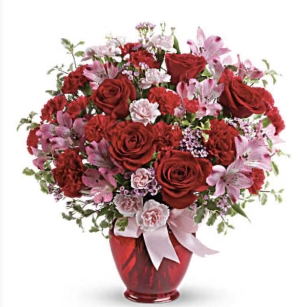 Red and pink flower arrangement in a red vase with a ribbon