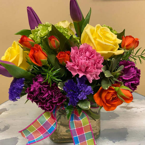 Colorful bouquet of roses, carnations, and tulips in a glass vase with a plaid ribbon