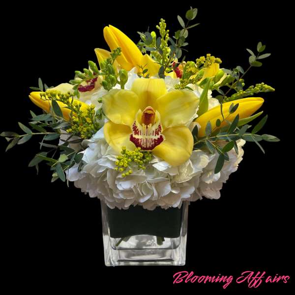 Yellow orchids and white hydrangeas in a clear square vase