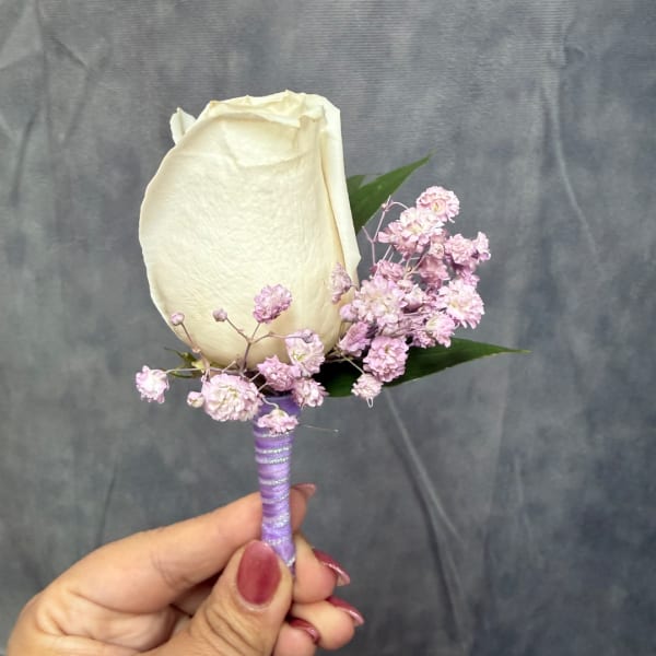 White rose boutonniere with small pink filler flowers and a purple wrapped stem