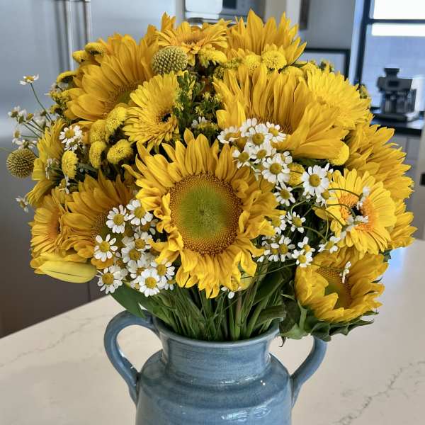 Bouquet of yellow sunflowers and white daisies in a blue ceramic vase