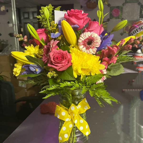 Colorful mixed bouquet in a glass vase with a yellow polka-dot ribbon