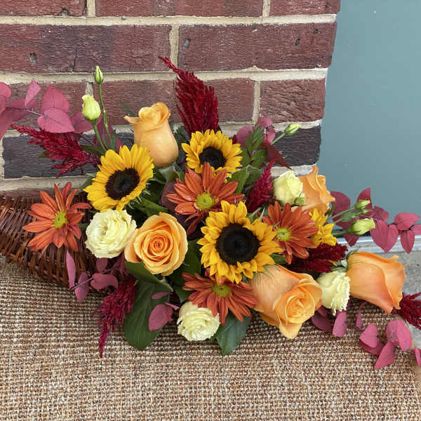 Orange roses and sunflowers in a wicker basket with pink foliage