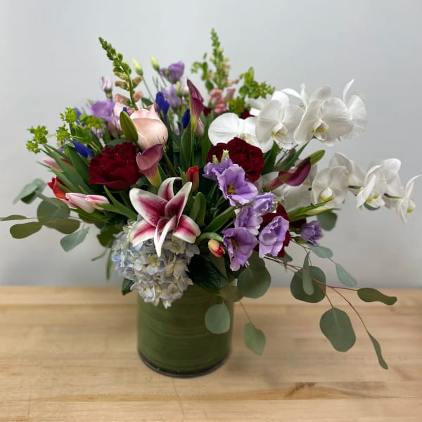 Mixed bouquet in a green glass vase with white orchids, lilies, and purple blooms