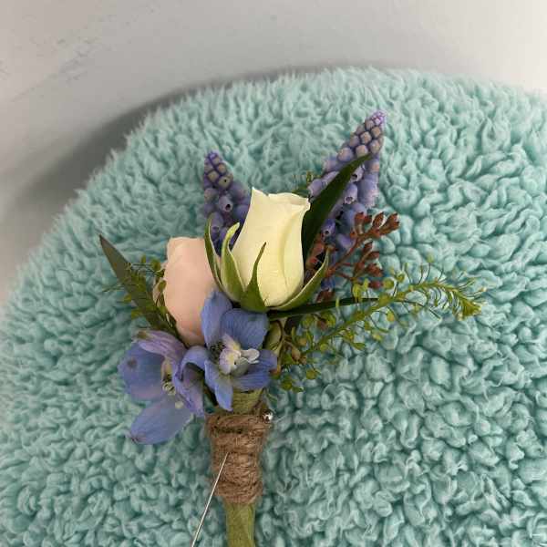 Small boutonniere with a white rose, blue flowers, and purple accents