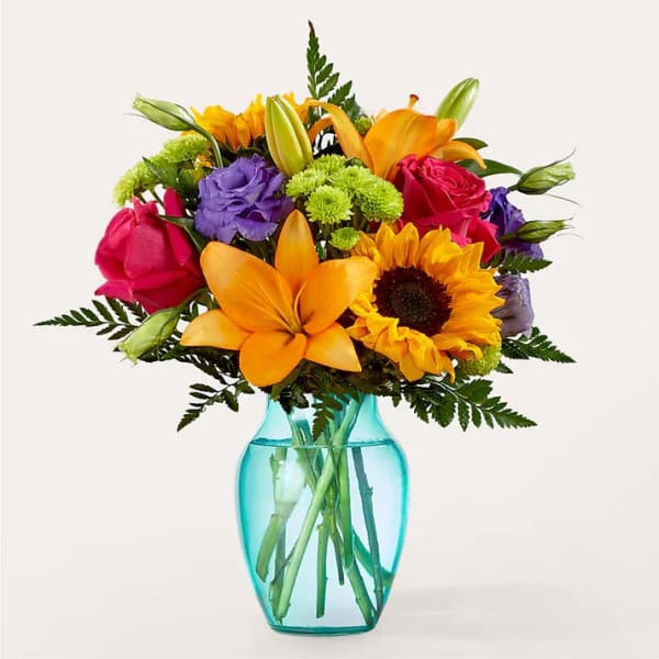 Mixed bouquet of roses, lilies, and a sunflower in a blue glass vase