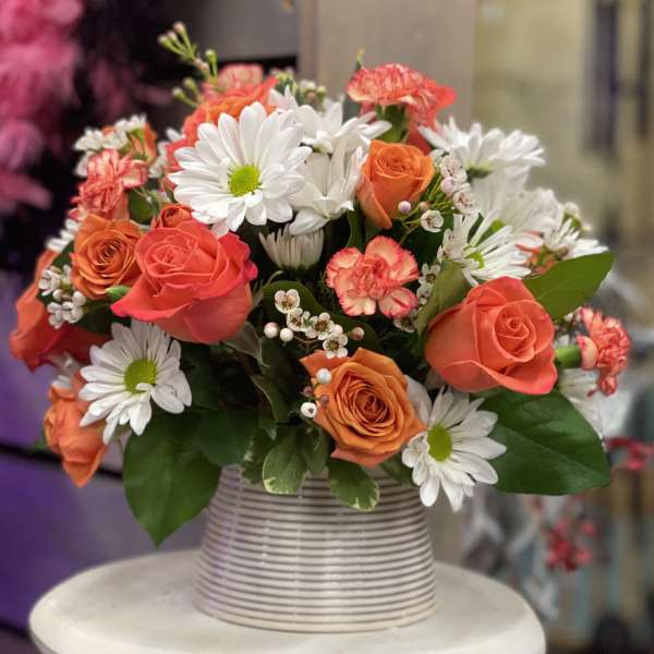 Bouquet of orange roses and white daisies in a striped vase