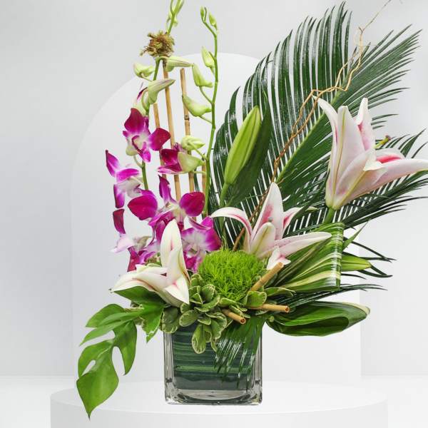Tropical floral arrangement with orchids and lilies in a glass vase
