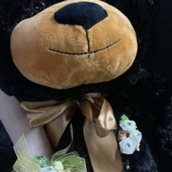 Black teddy bear with a gold bow and floral wrist corsage