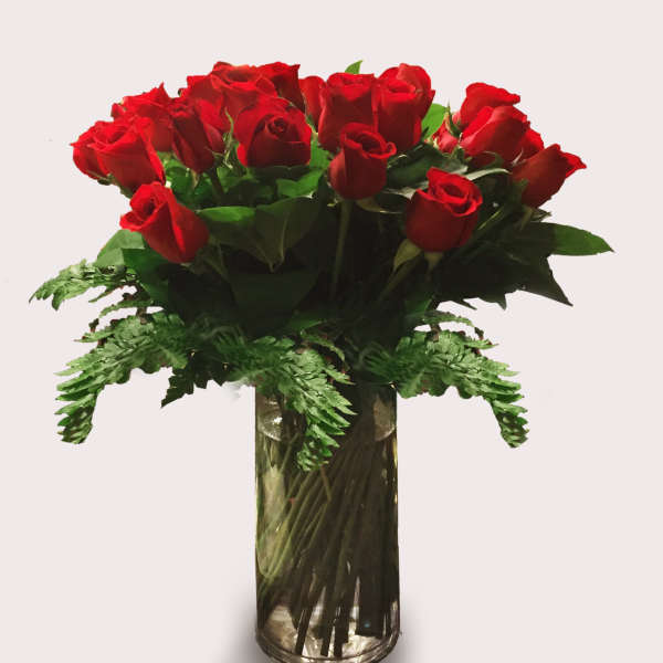 Red roses arranged in a clear glass vase with fern accents