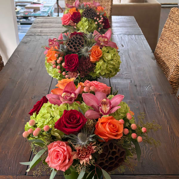Three colorful floral centerpieces with roses, orchids, and hydrangeas on a table