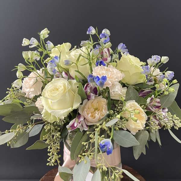 Bouquet of cream roses, pale peach blooms, and blue accents in a vase