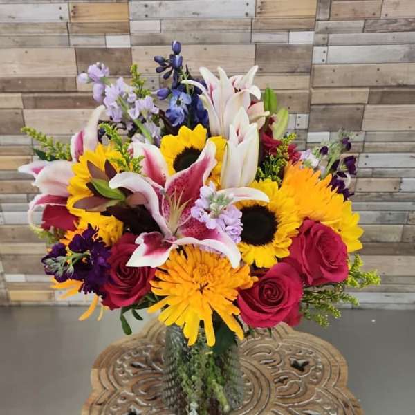 Mixed bouquet with lilies, sunflowers, and roses in a glass vase