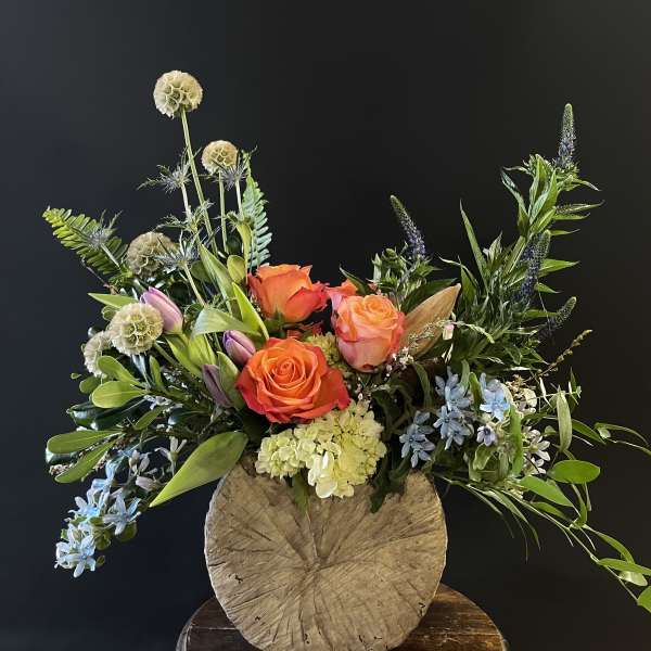 Mixed bouquet with orange roses, lilies, and blue flowers in a rustic vase