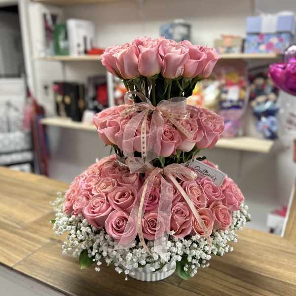 Tiered arrangement of pink roses with white baby's breath in a white container