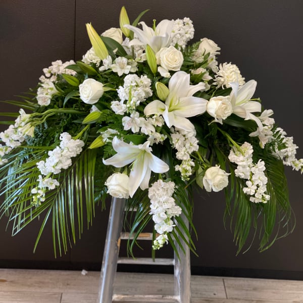 White floral funeral spray with lilies and roses on a stand