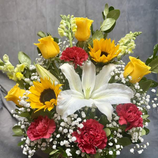 Basket arrangement with white lily, yellow roses, sunflowers, and red carnations