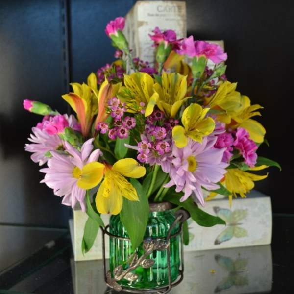 Colorful bouquet of pink, yellow, and lavender flowers in a green glass vase