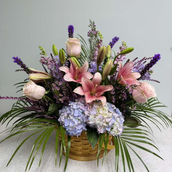 Basket arrangement with pink lilies, roses, and blue hydrangeas