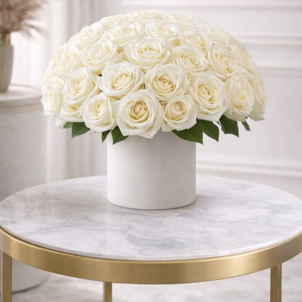Dome of cream roses arranged in a white round vase on a marble table